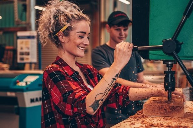 Das Foto zegut eine Holzmechanikerin an der Bohrmaschine