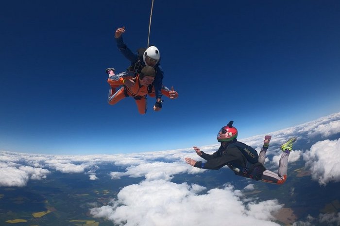 Das Foto zeigt zwei Menschen beim Tandemsprung und einn Einzelnen Springer im freien Fall