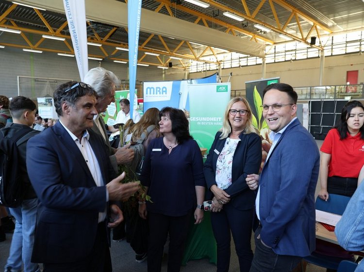 Das Foto zeigt die Messehalle, im Vordergrund eine Gruppe Menschen im Gesprächgrund eine Menschengruppe