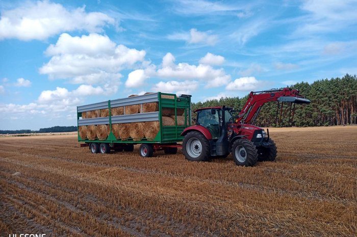 Das Foto zeigt einen Traktor mit Hänger, der Strohballen transportiert