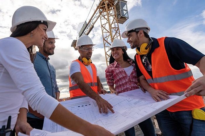 Das Foto zeigt vier Menschen um einen Bauplan auf einer Baustelle