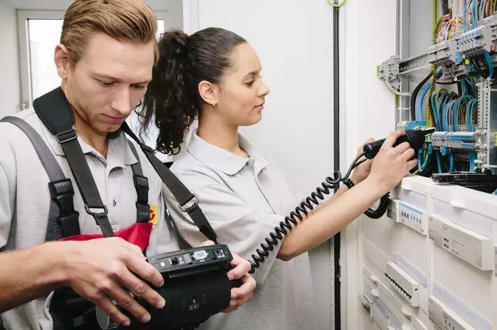 Das Foto zeigt zwei Elektroniker-Azubis beim Check eines Schaltkastens