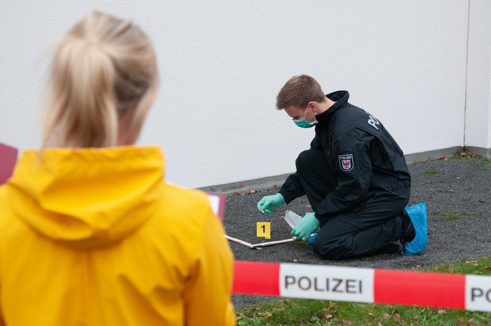 Das Foto zeigt einen Mann in Uniform bei der Spurensuche und eine Beobachterin