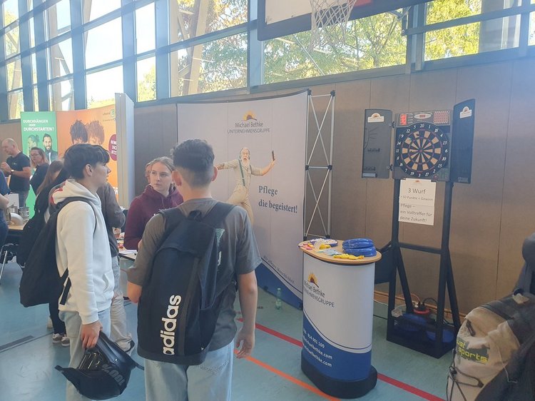 Das Foto zeigt Schüler im Gespräch vor einer DartScheibe an einem Messestand